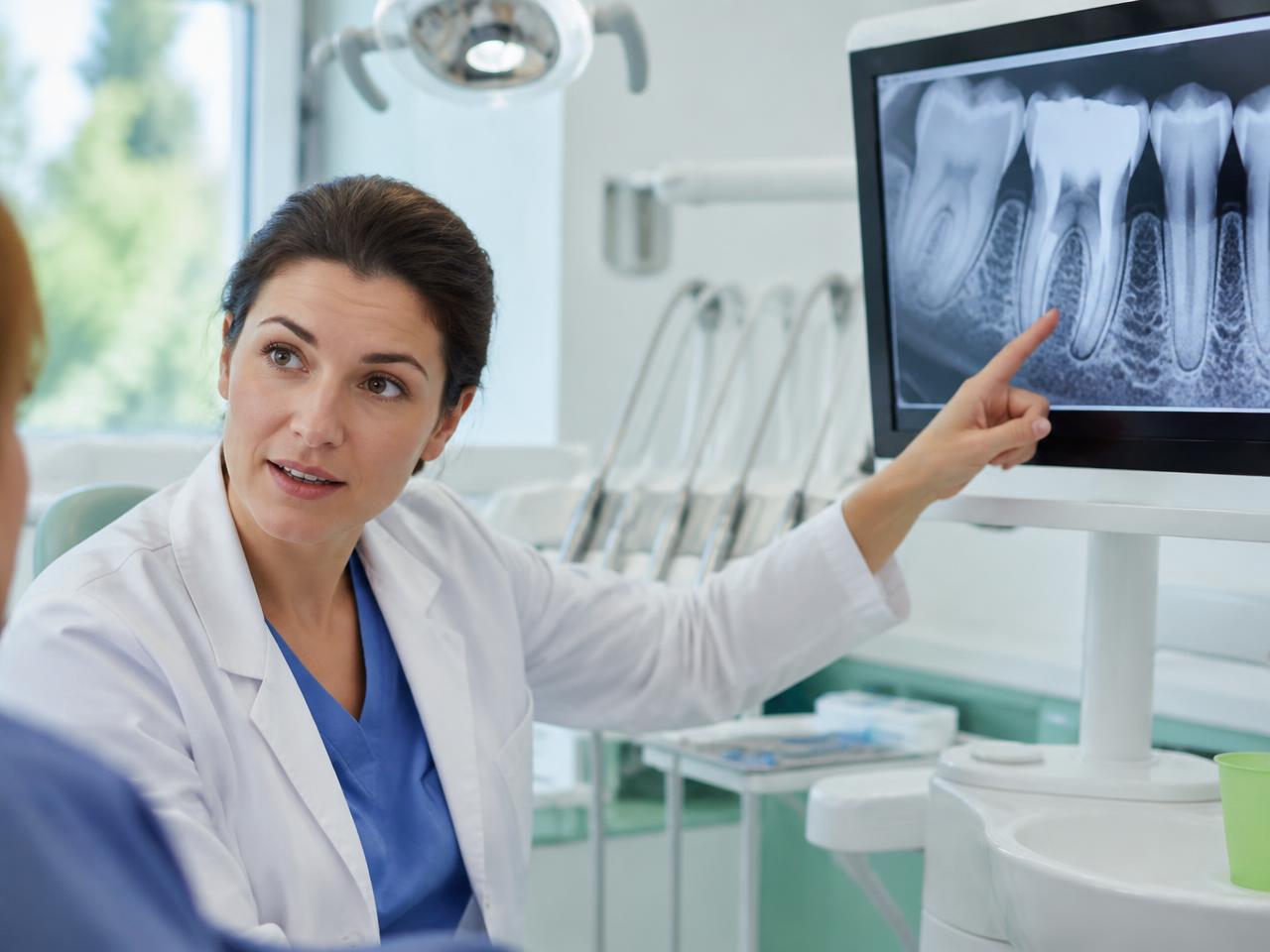 Une dentiste montre une radiographie dentaire affichée sur un écran.